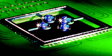 A photograph of a PCR chip soldered to a printed circuit board (PCB) with a square microscope glass cover slip. Four water-based samples, each with a volume of 1 μL, are placed on the glass and covered with 5 μL of mineral oil. The samples contain blue dye for easier visualization. Due to the soldering technique, we have achieved low resistance between the PCB and the chip as well as robust mechanical connection. Also, handling the whole PCB is much simpler than dealing with bare silicon chips.