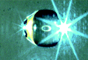 Levitated droplet of styrene illuminated with blue laser beam. The horizontal directed light is mainly scattered at the equator of the droplet. An additional ring illumination is reflected on the center of the droplet surface.